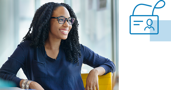 A newly hired young woman sits in an office and smiles at an offscreen HR Manager; next to her is an employee badge