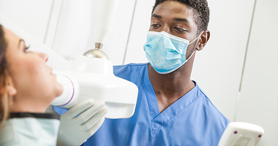 A dental hygienist adjusts the position of the x-ray machine to better capture an x-ray of a patient's teeth