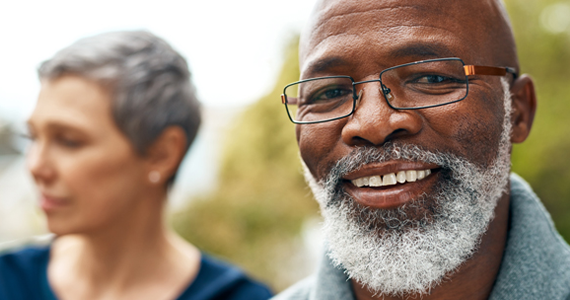 A healthy-looking older man smiles feeling secure with his life insurance choices. His partner can be seen in the background