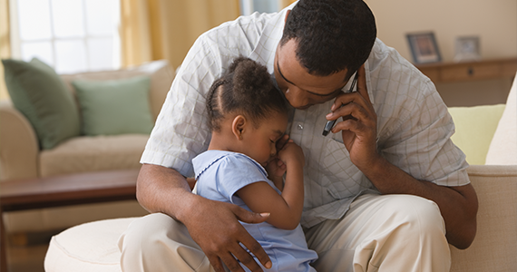 A father comforts his young child in their home as he talks to a Mortensen representative about short-term disability options