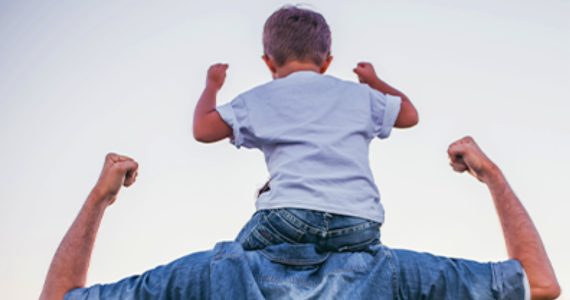 A child sits on his father's shoulders and both are flexing their biceps